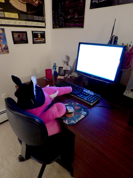 photograph of a large pink stuffed elephant wearing a hat with cat ears, posed to look like it is sitting at his desk using his computer